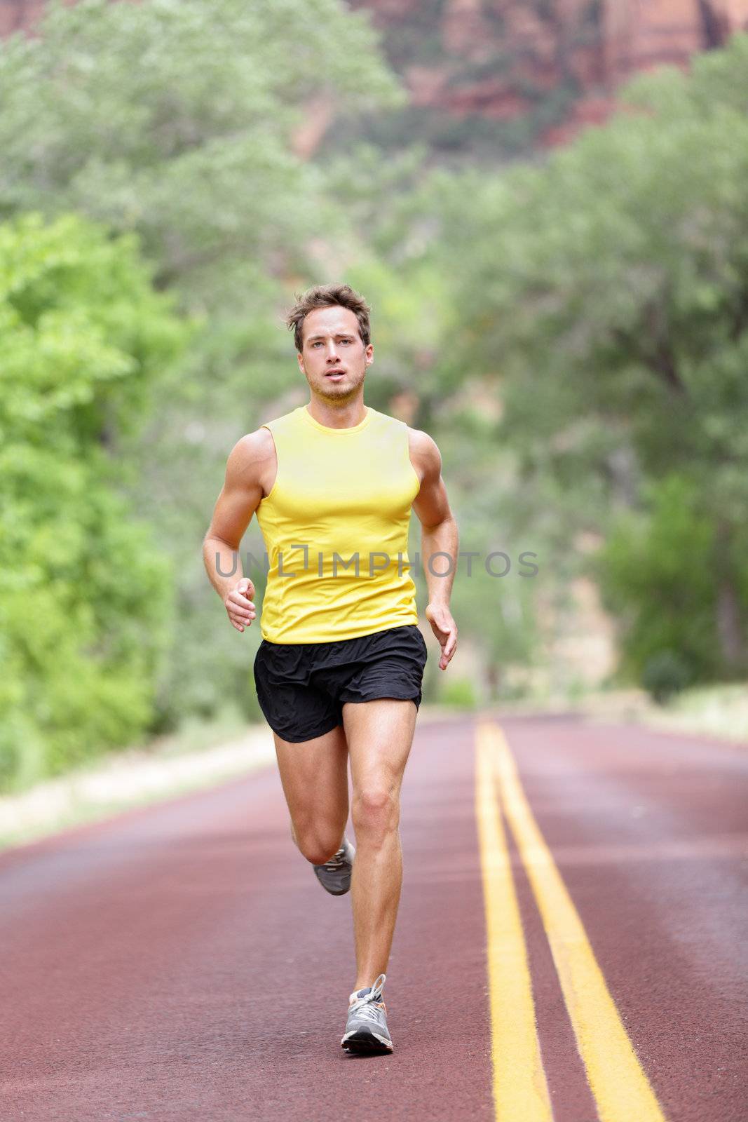 Runner man running with concentration, determination and strength in full length on road. Fit male sport fitness model sprinting outdoors.