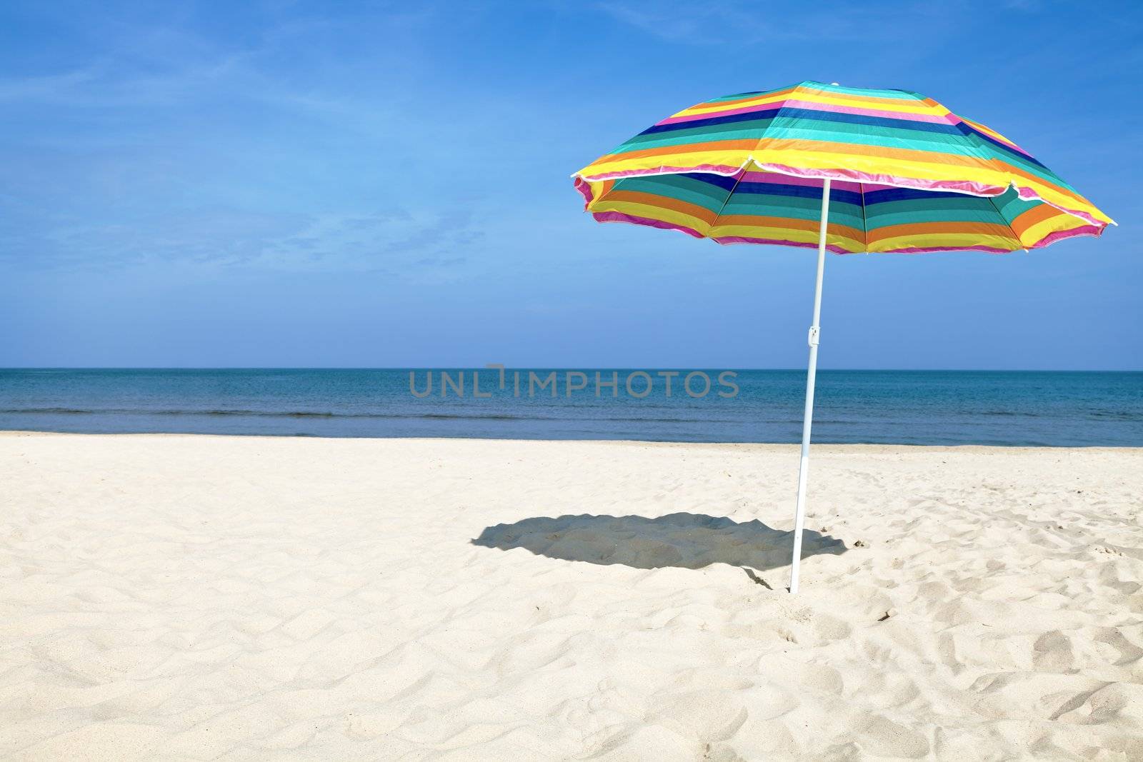 Colorful beach umbrella on the sandy beach on summer day. Blue sky and sea in the background