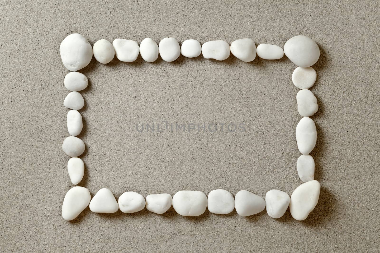 Frame of white pebbles on sand background with copy space