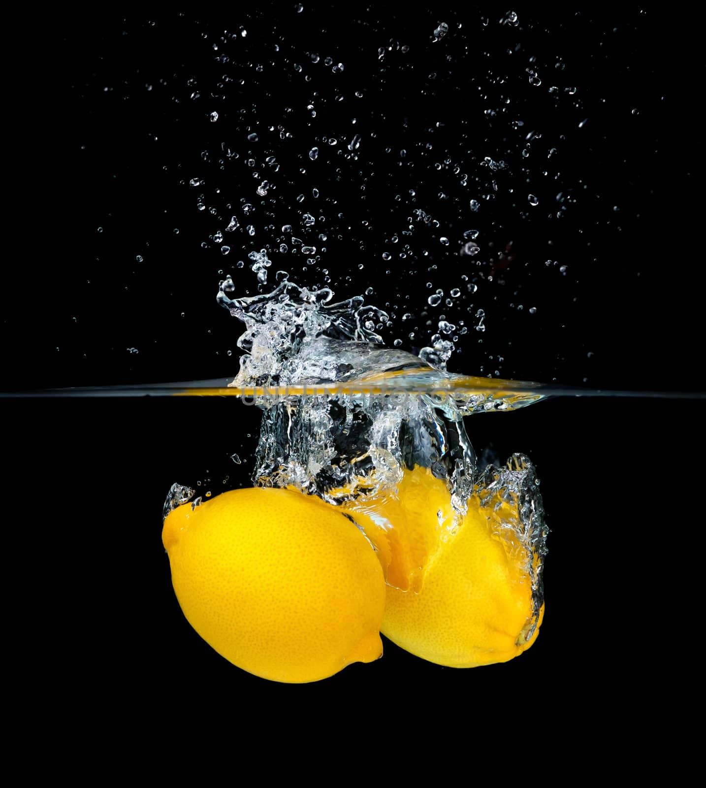 Two fresh lemons falling into water, isolated on black background