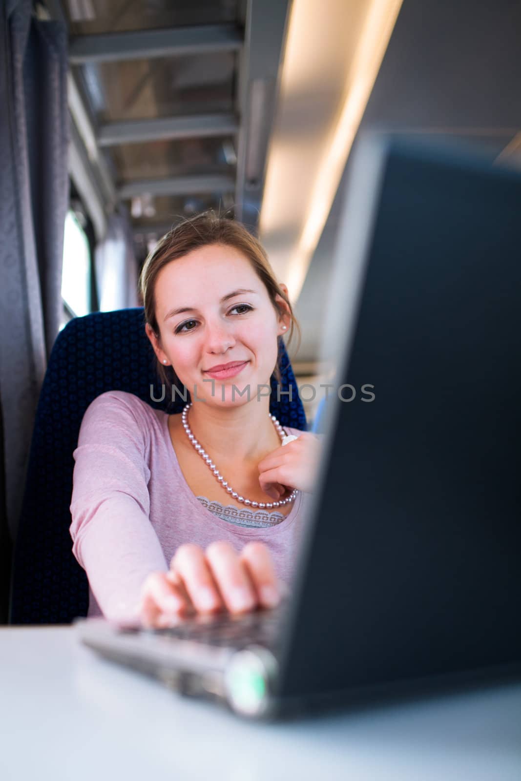 Young woman using her laptop computer while on the train (shallow DOF; color toned image)