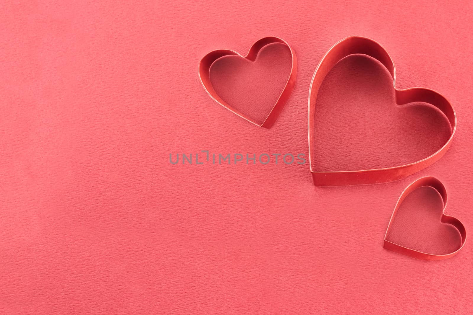 Three heart shaped cookie cutters over a red background.