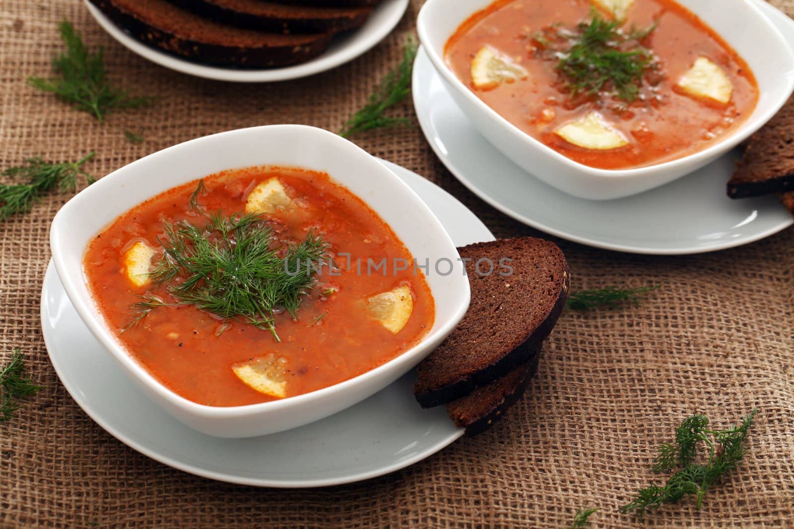 Image of bowls of hot red soup served with bread on a beige tablecloth
