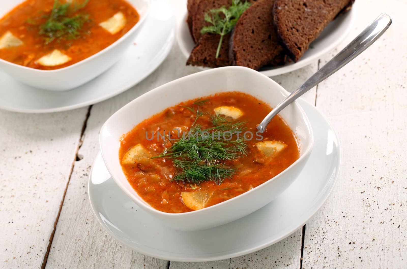 Image of bowl of hot red soup and black bread on white wooden table