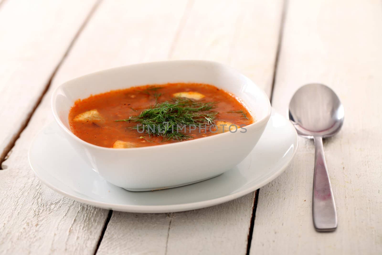 Image of bowl of hot red soup isolated on white wooden table