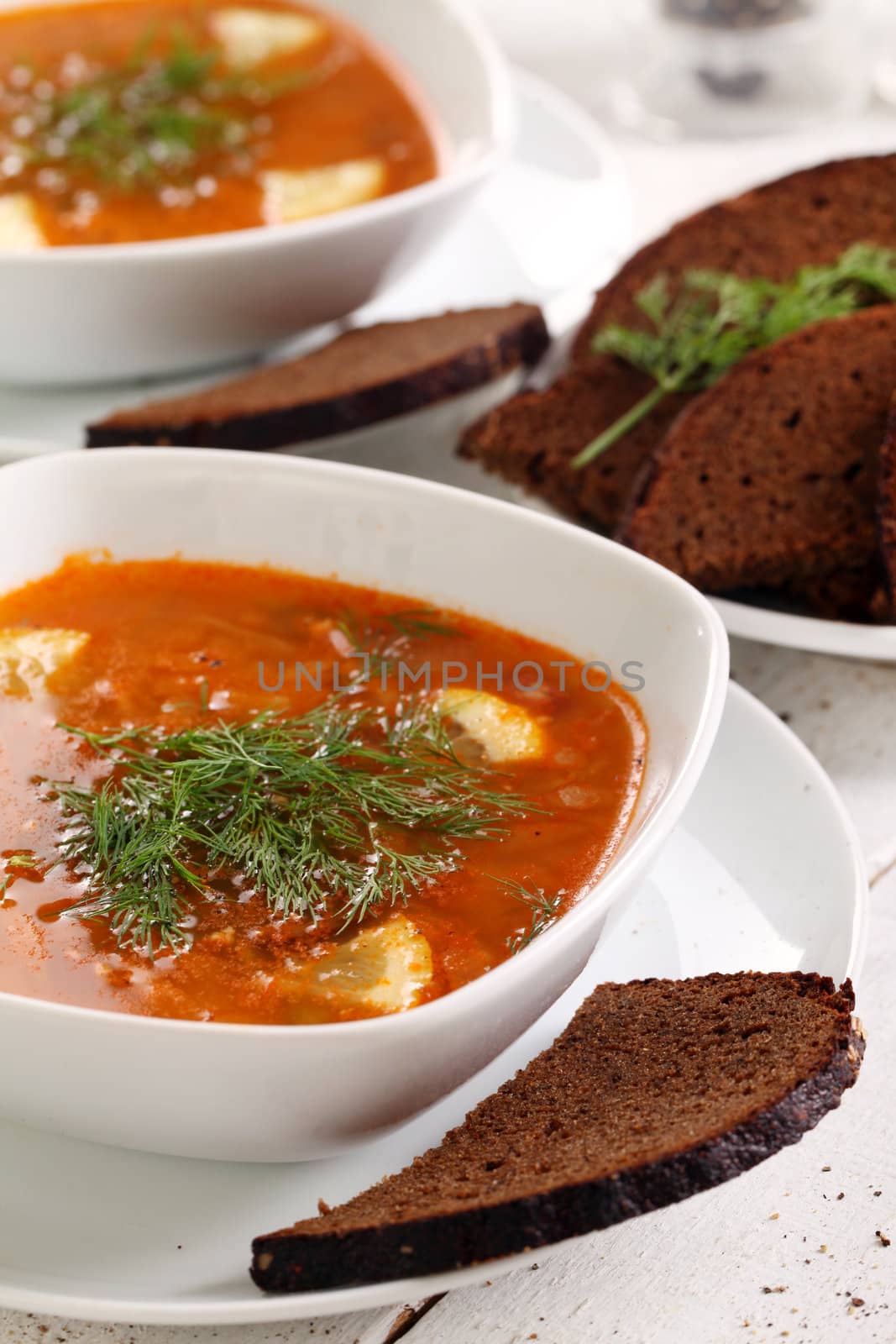 Image of bowl of hot red soup and black bread on white wooden table