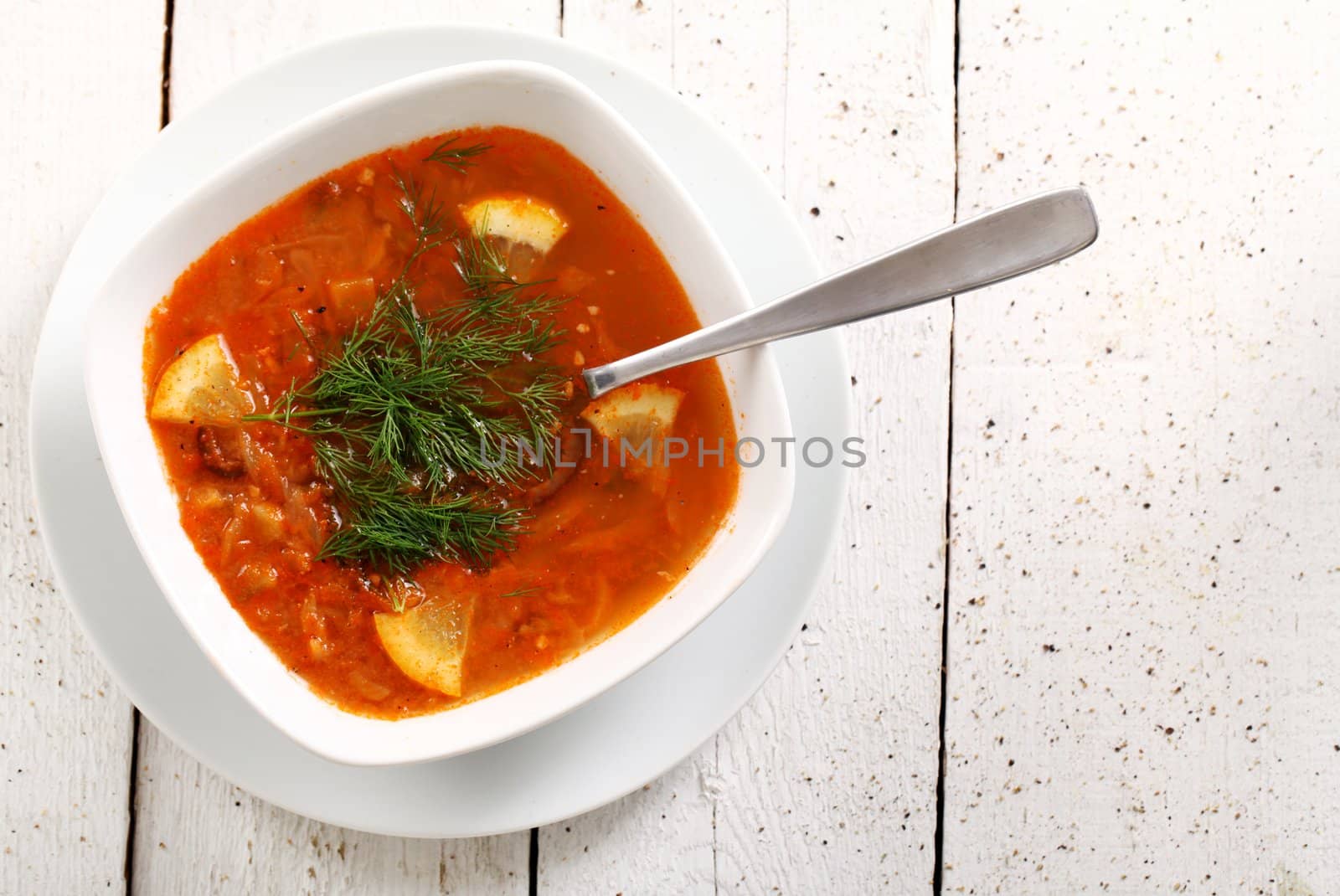 Image of bowl of hot red soup isolated on white wooden table