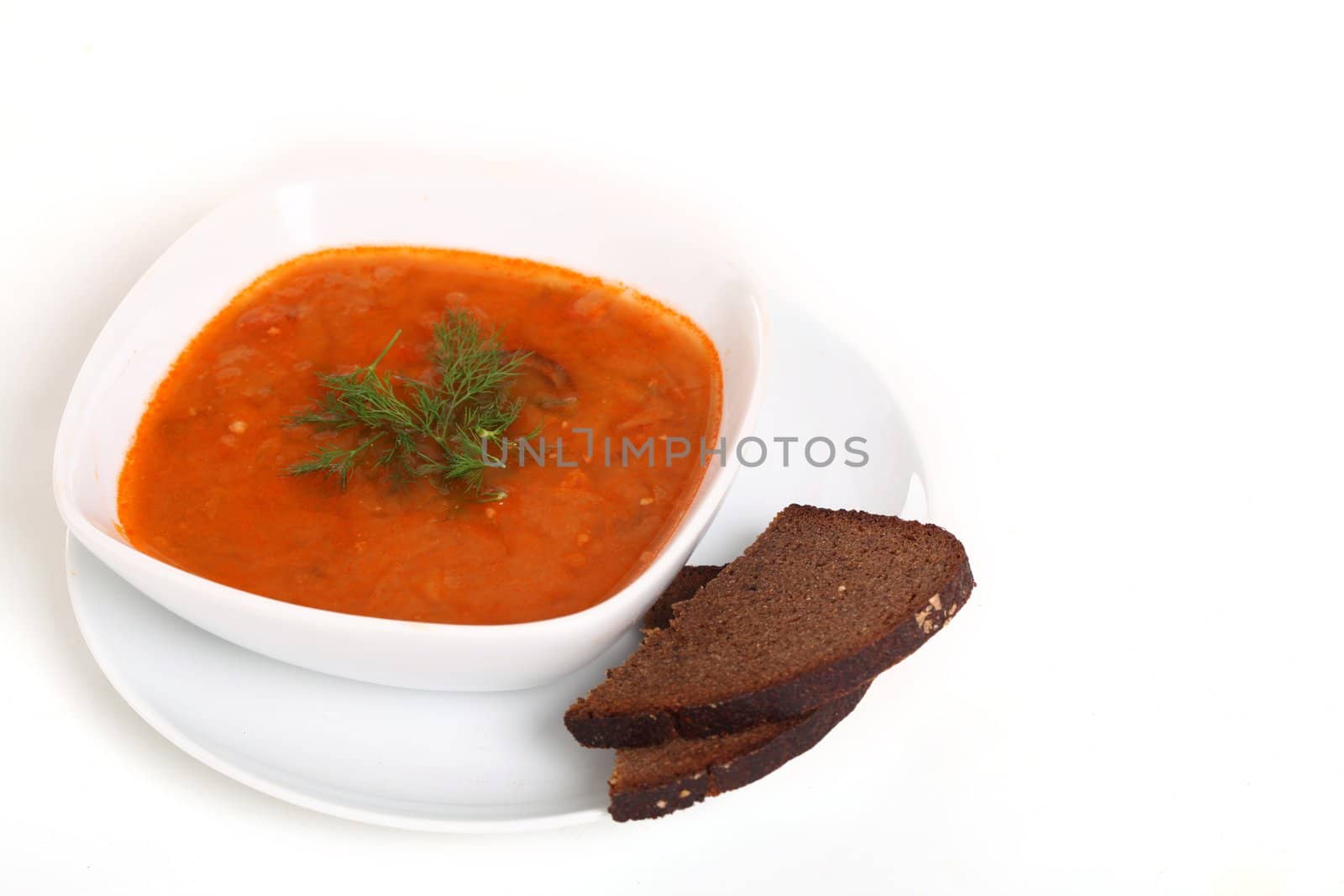 Image of bowl of hot red soup and piece of black bread isolated on white background