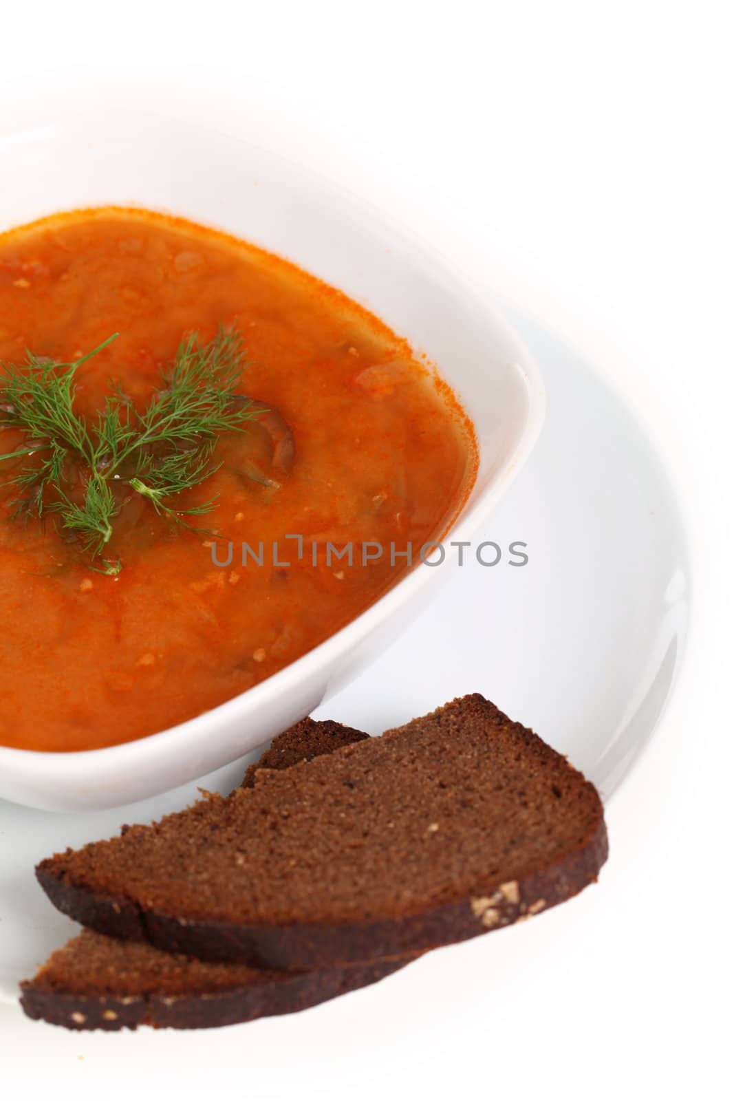 Image of bowl of hot red soup and piece of black bread isolated on white background