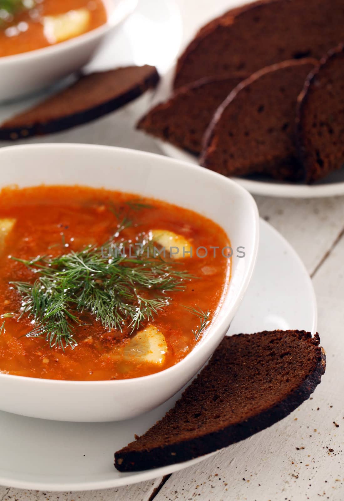 Image of bowl of hot red soup and black bread on white wooden table