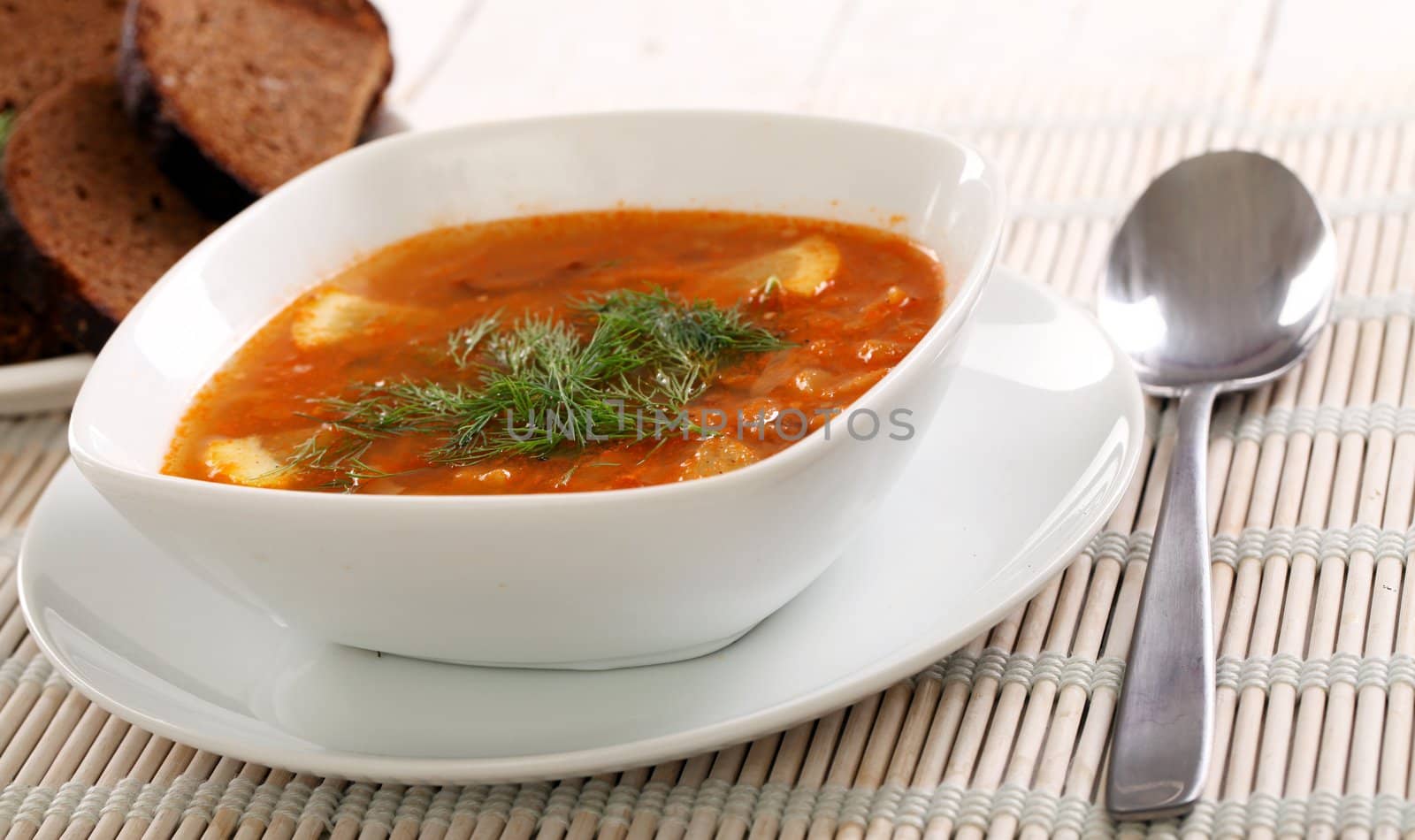 Image of bowl of hot red soup isolated on white wooden table