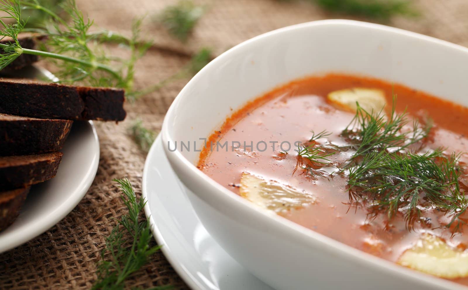 Image of bowls of hot red soup served with bread on a beige tablecloth