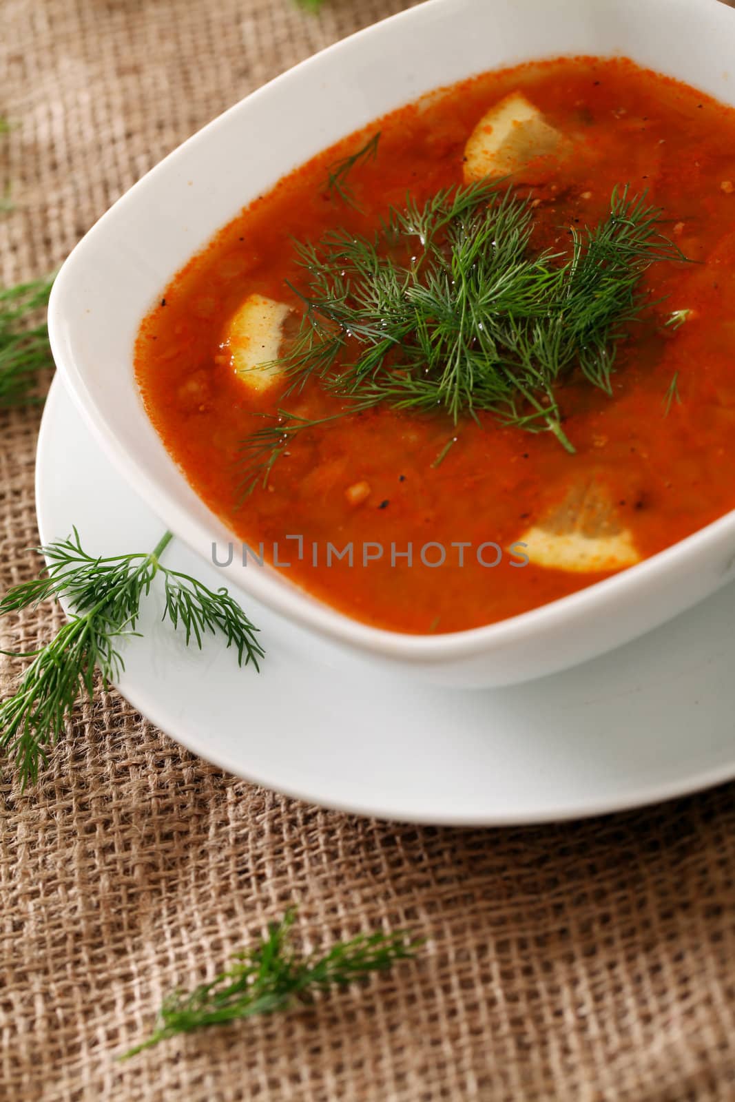 Image of bowl of hot red soup served with parsley on a beige tablecloth