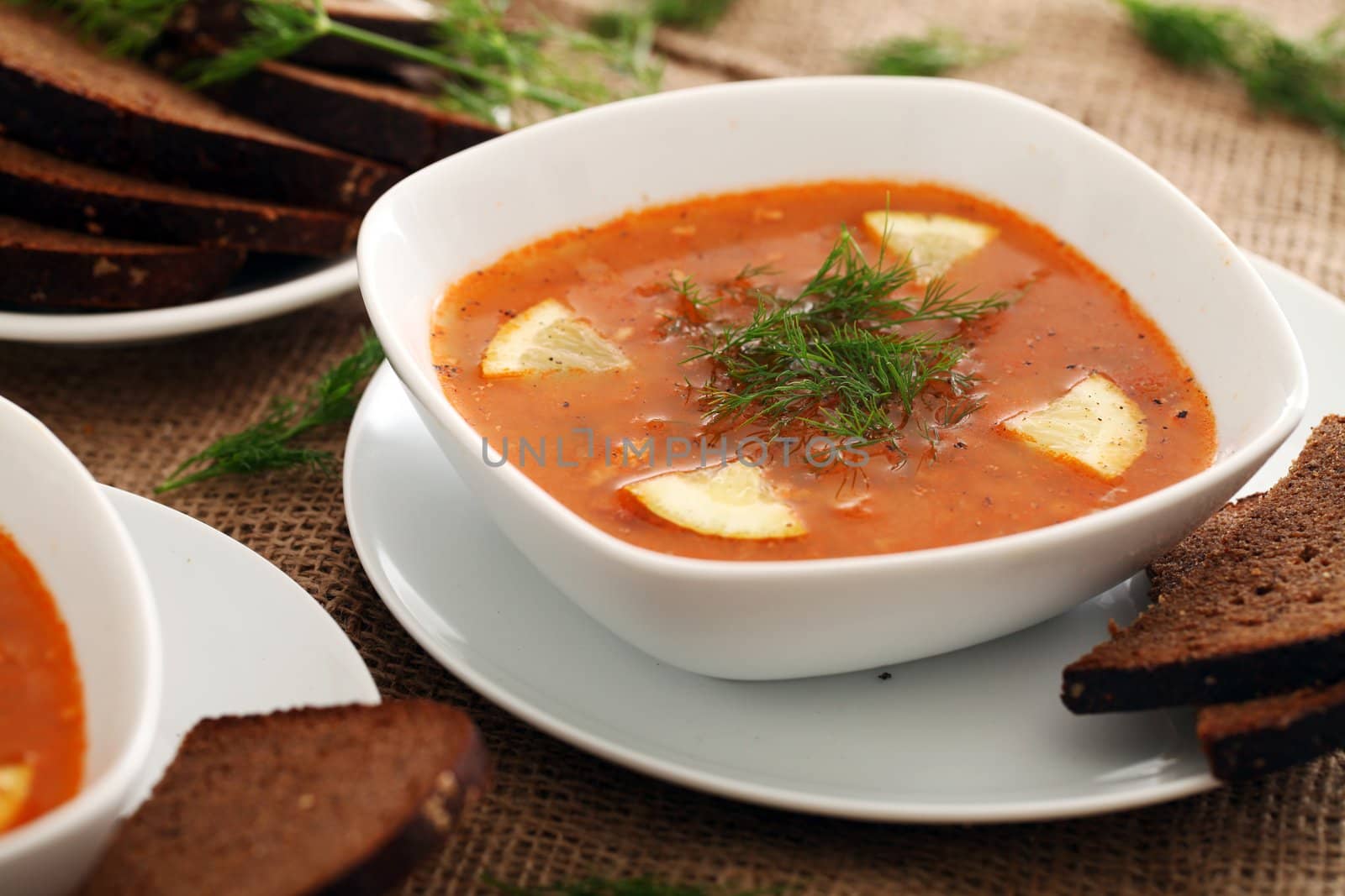 Image of bowls of hot red soup served with bread on a beige tablecloth