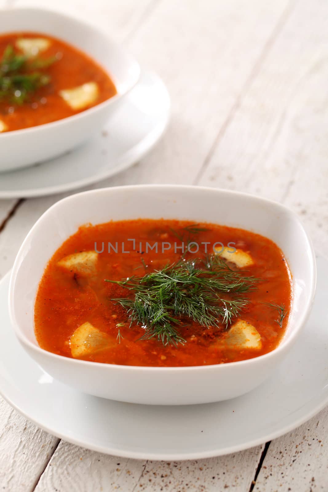 Image of two bowls of hot red soup isolated on white wooden table