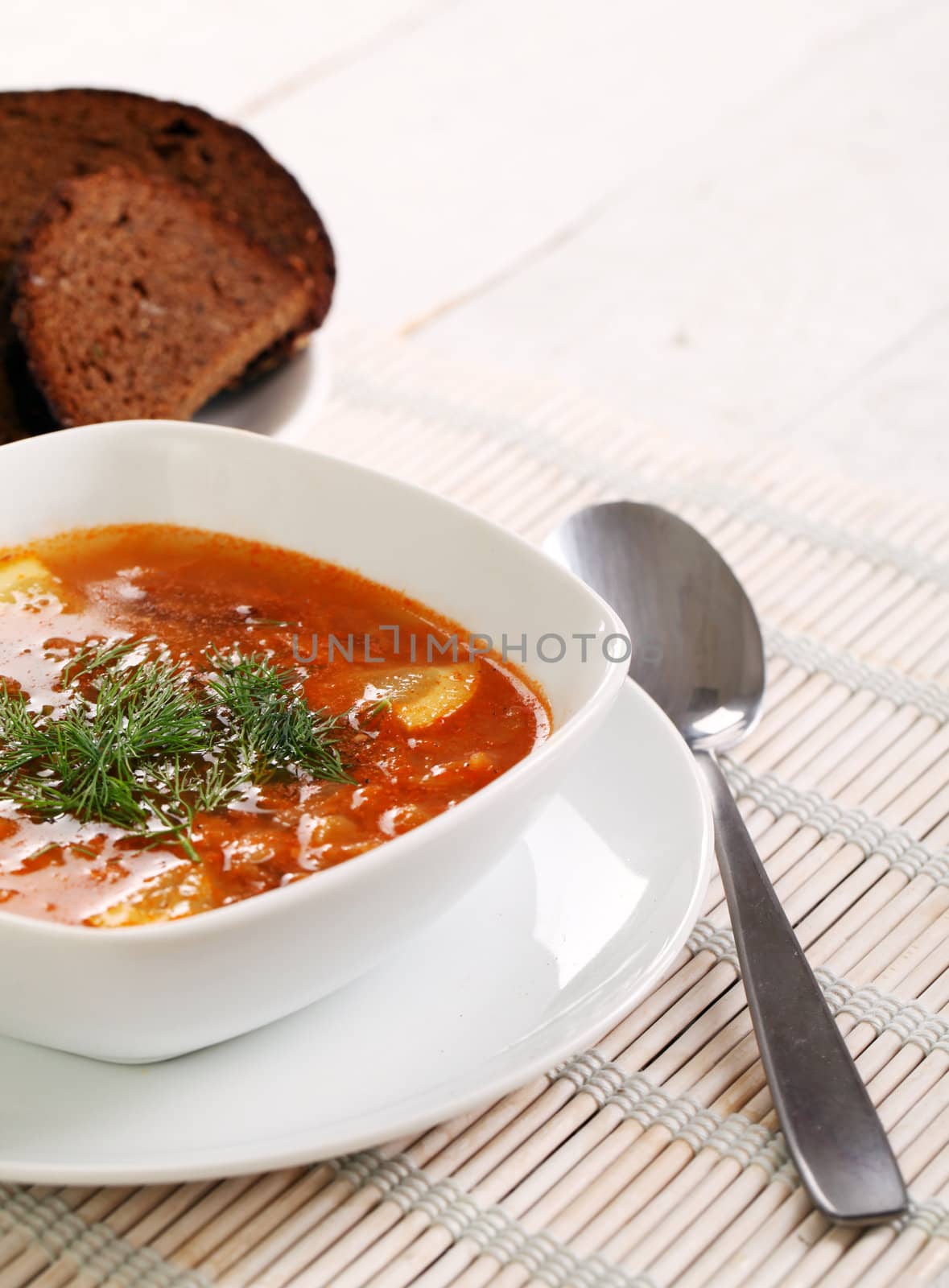 Image of bowl of hot red soup isolated on white wooden table