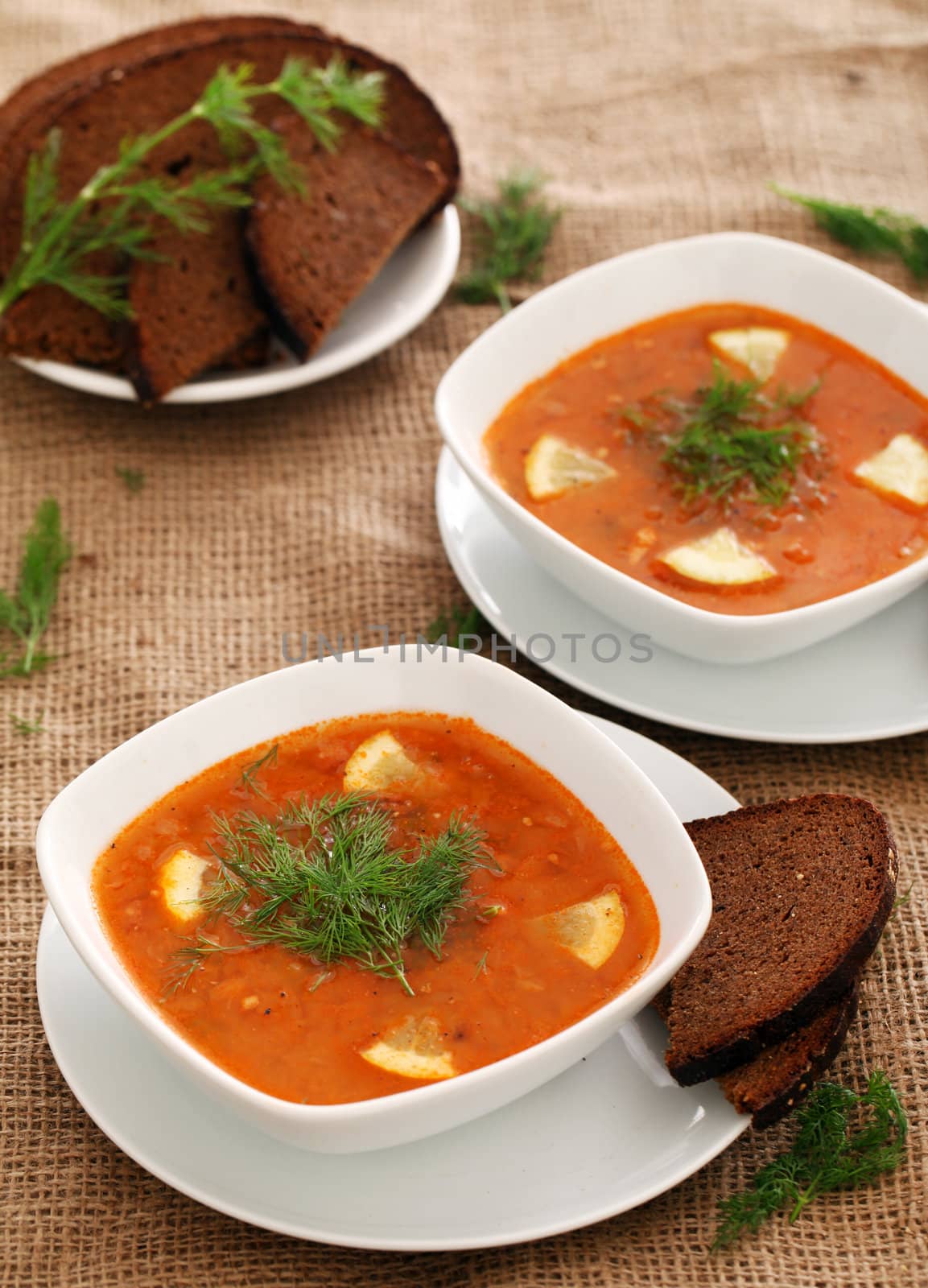 Image of bowls of hot red soup served with bread on a beige tablecloth