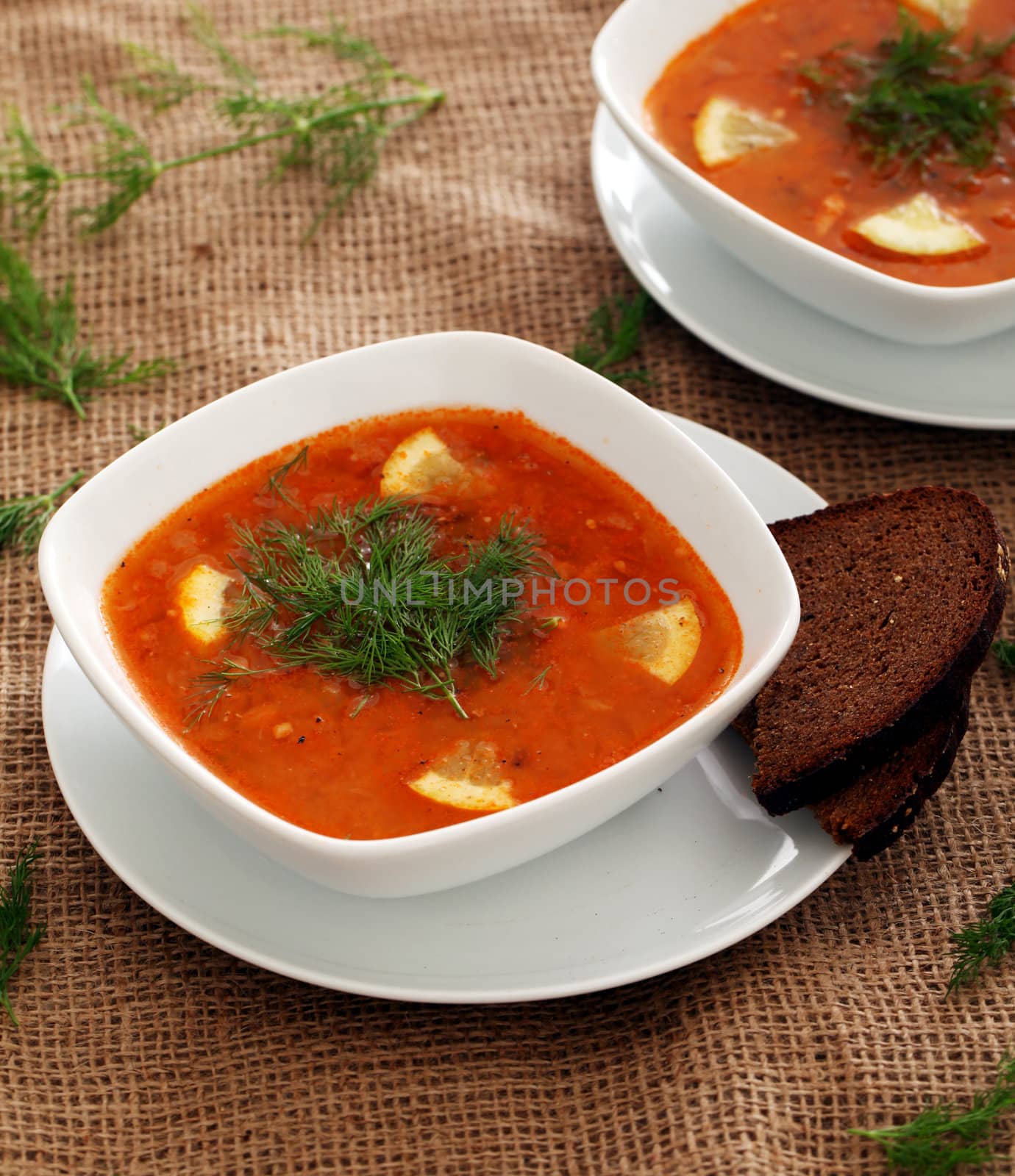 Image of bowls of hot red soup served with bread on a beige tablecloth