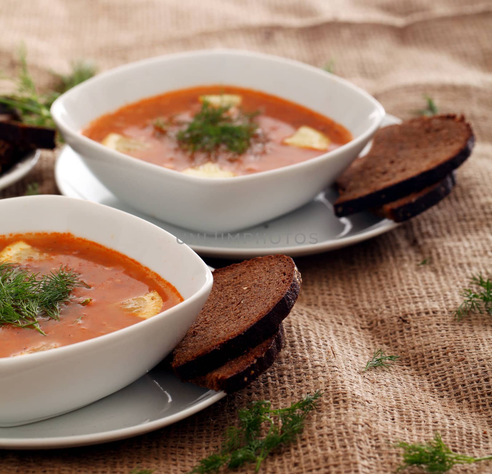 Image of bowls of hot red soup served with bread on a beige tablecloth