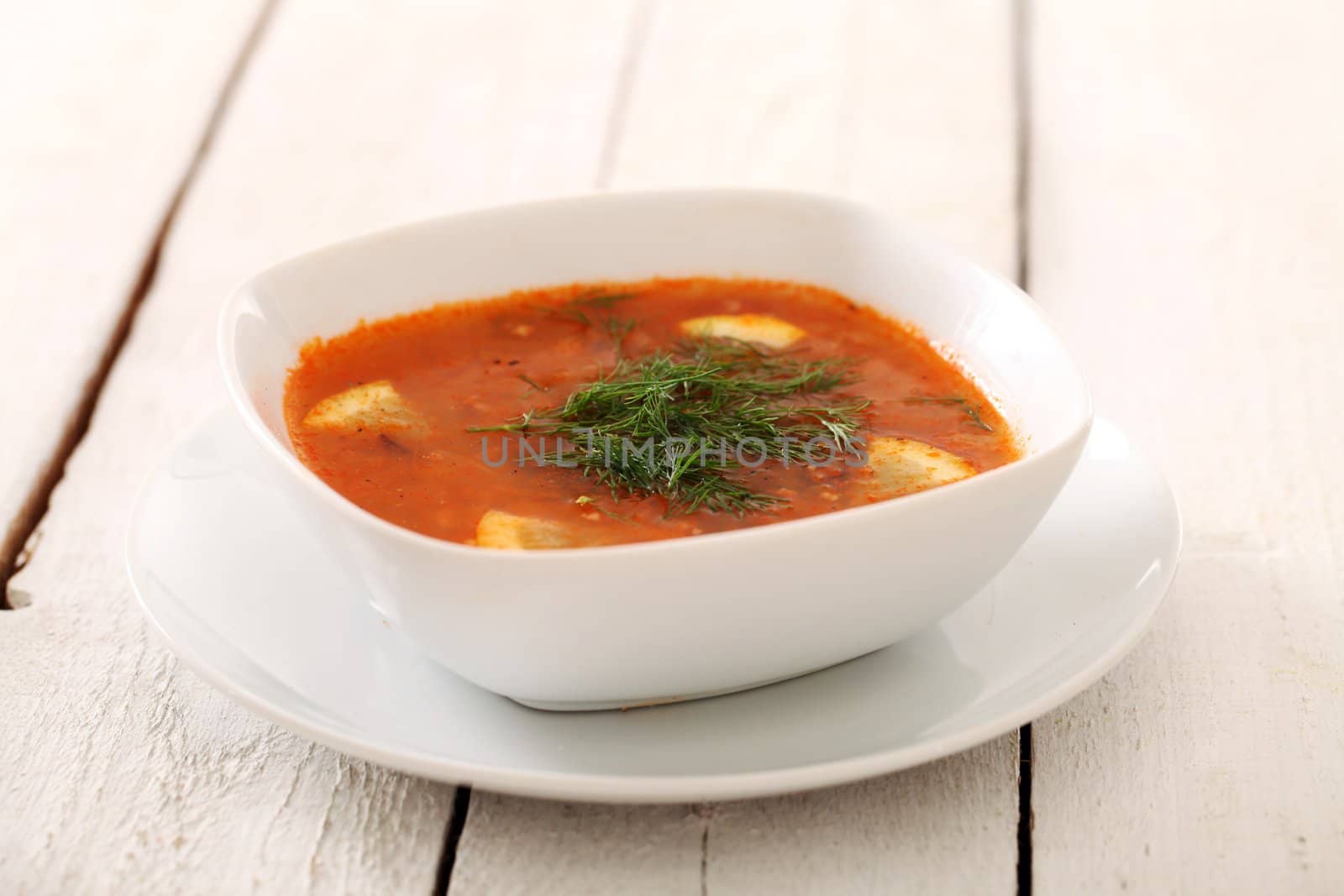 Image of bowl of hot red soup isolated on white wooden table