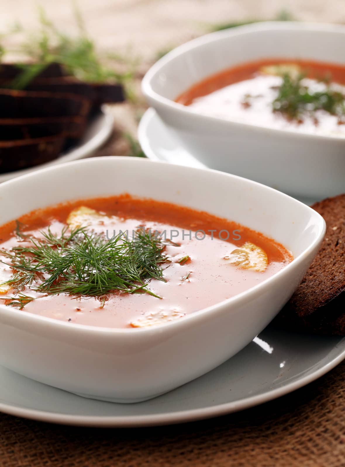 Image of bowls of hot red soup served with bread on a beige tablecloth