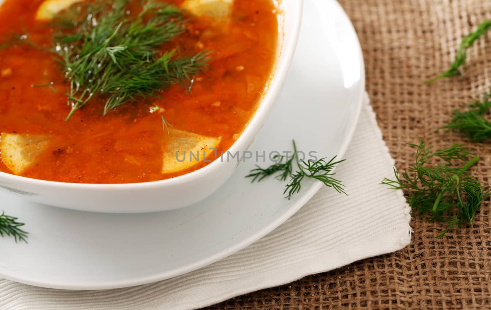 Image of bowl of hot red soup served with parsley on brown tablecloth