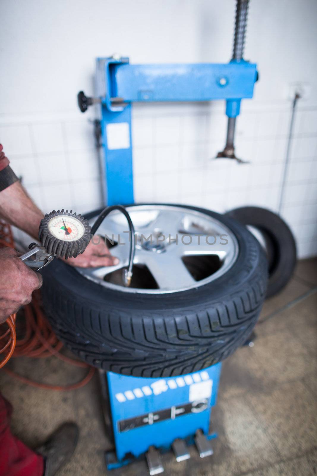 Auto mechanic in a garage checking the air pressure in a tyre with a pressure gauge  (shallow DOF; color toned image)