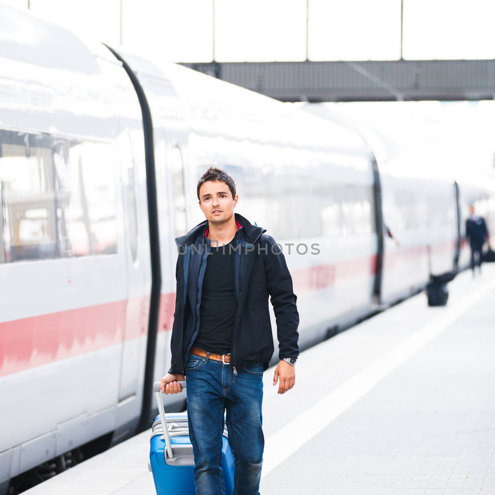 Just arrived: handsome young man walking along a platform at a modern train station