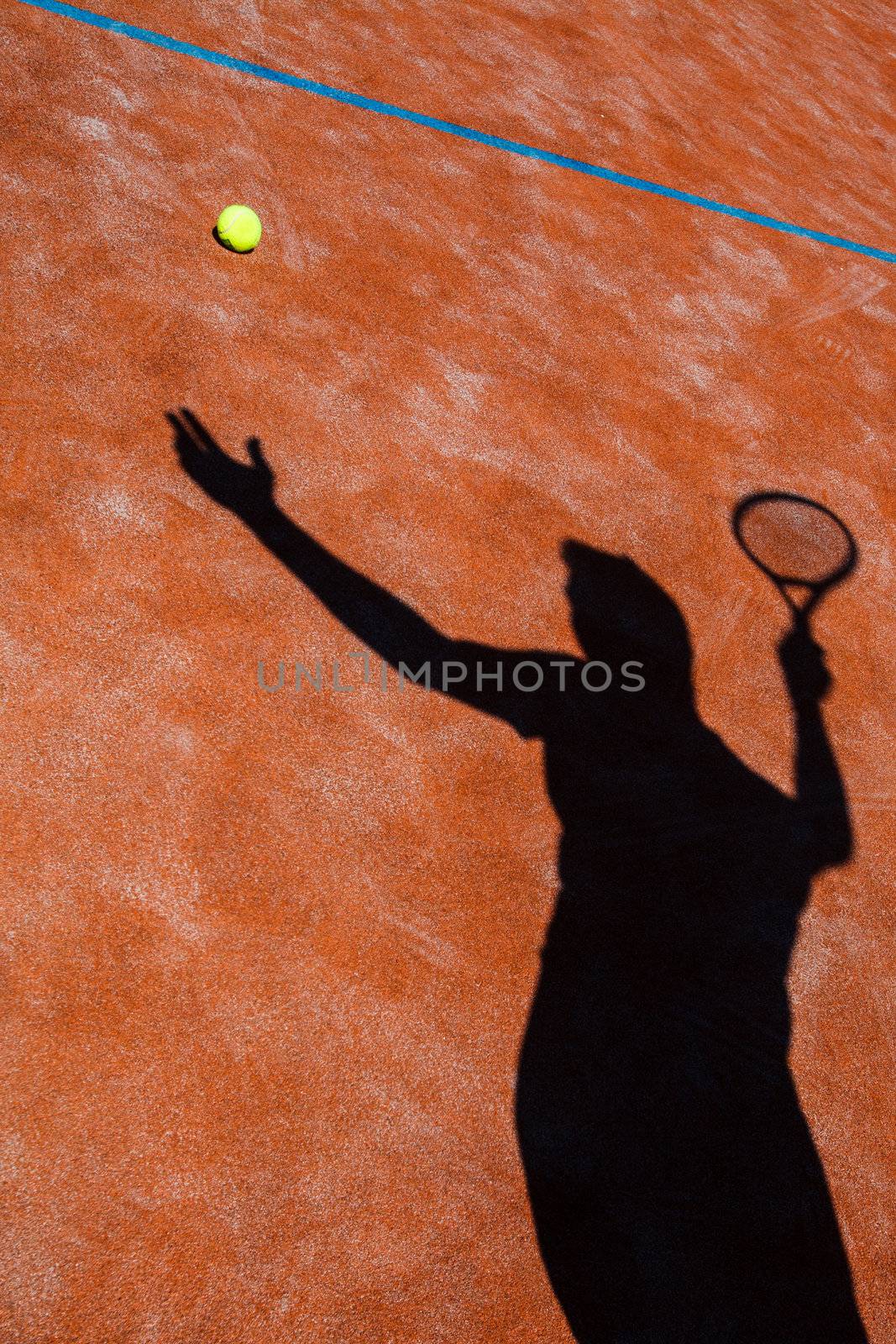 shadow of a tennis player in action on a tennis court (conceptual image with a tennis ball lying on the court and the shadow of the player positioned in a way he seems to be playing it)