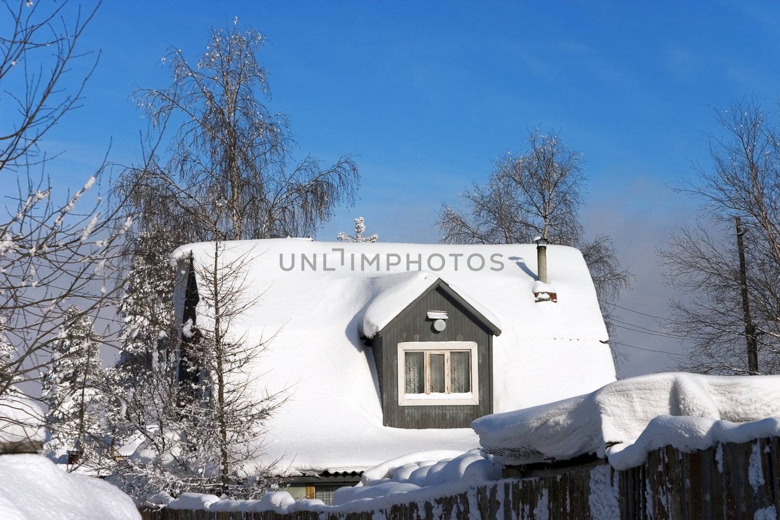 snow-covered roof of a village house on the background of bright blue sky