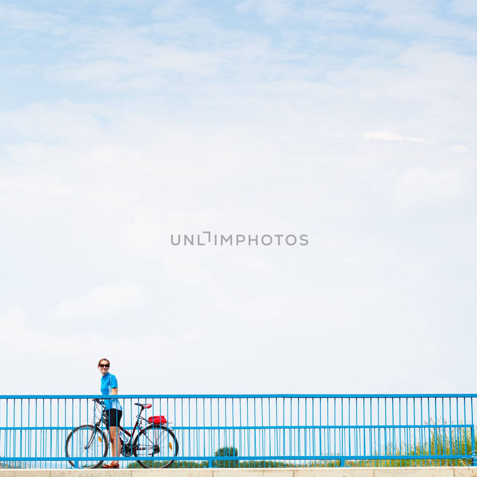 Background for poster or advertisment pertaining to cycling/sport/outdoor activities - female cyclist during a halt on a bridge against blue sky (color toned image)