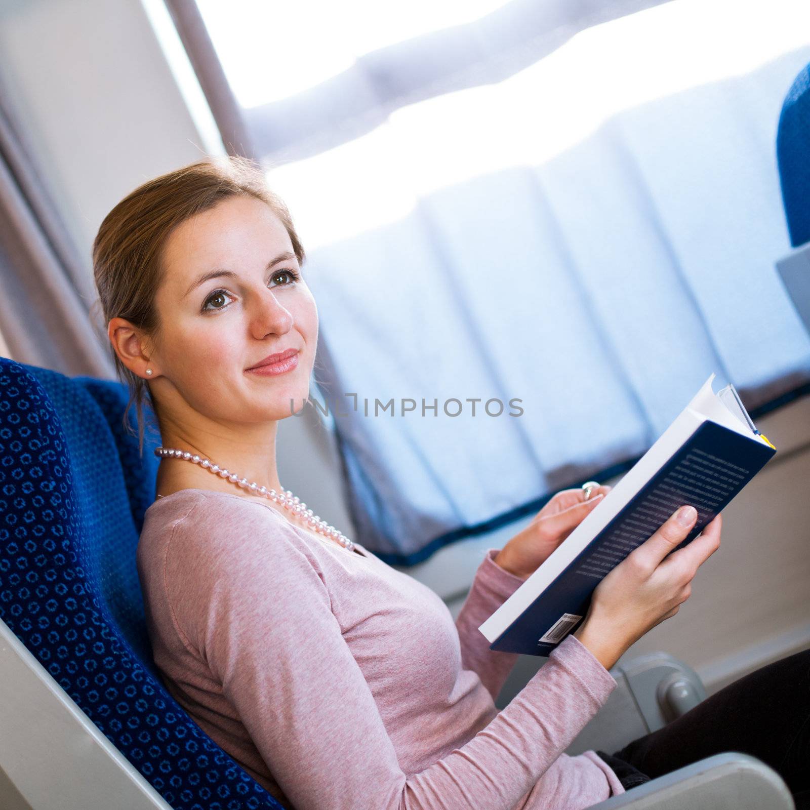 Young woman reading a book while on a train by viktor_cap
