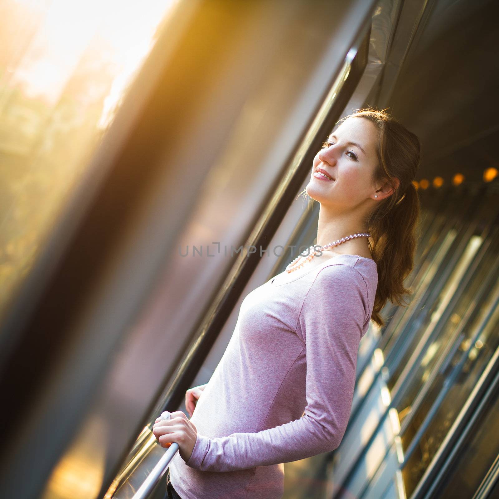 Young woman traveling by train, watching the passing country side while standing in the train corridor