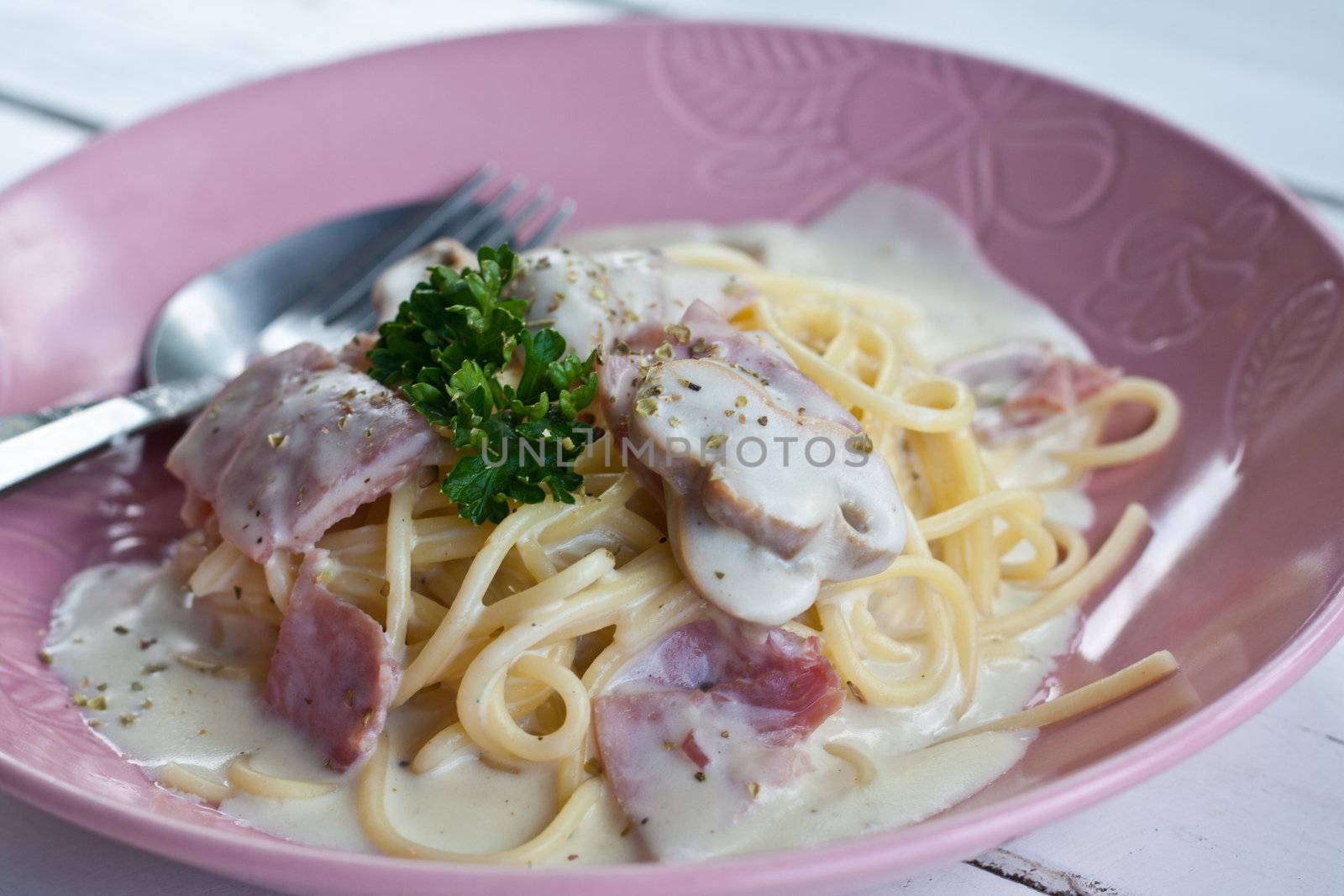 Spaghetti cream with bacon and parsley on pink dish.