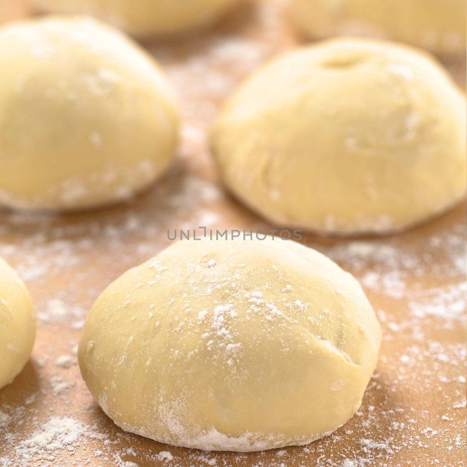 Small balls of fresh homemade pizza dough on floured wooden board  (Selective Focus, Focus one third into the first pizza dough) 