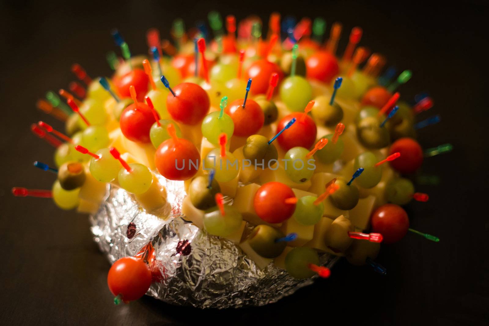 Cheese Hedgehog consisting of cheese sticks with tomatoes, olives and grapes into bread wrapped in silver foil