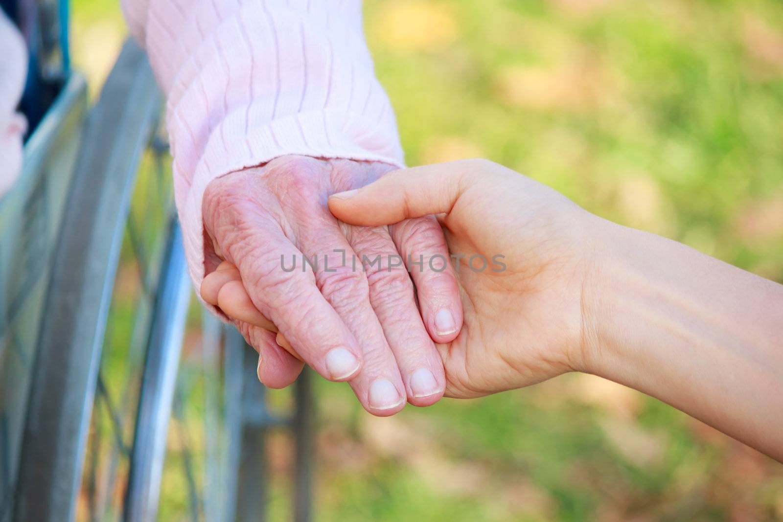 Senior Lady in Wheelchair Holding Hands with a Young Caretaker or Loved-one