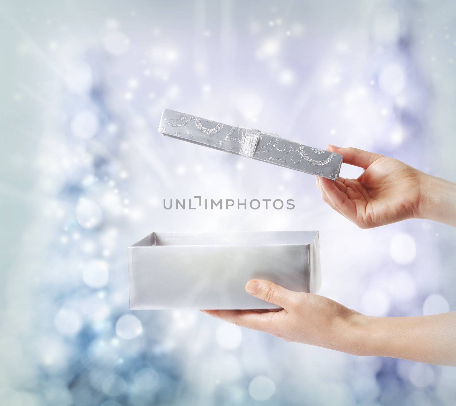 Woman opening a silver gift box on a blue holiday lights background 