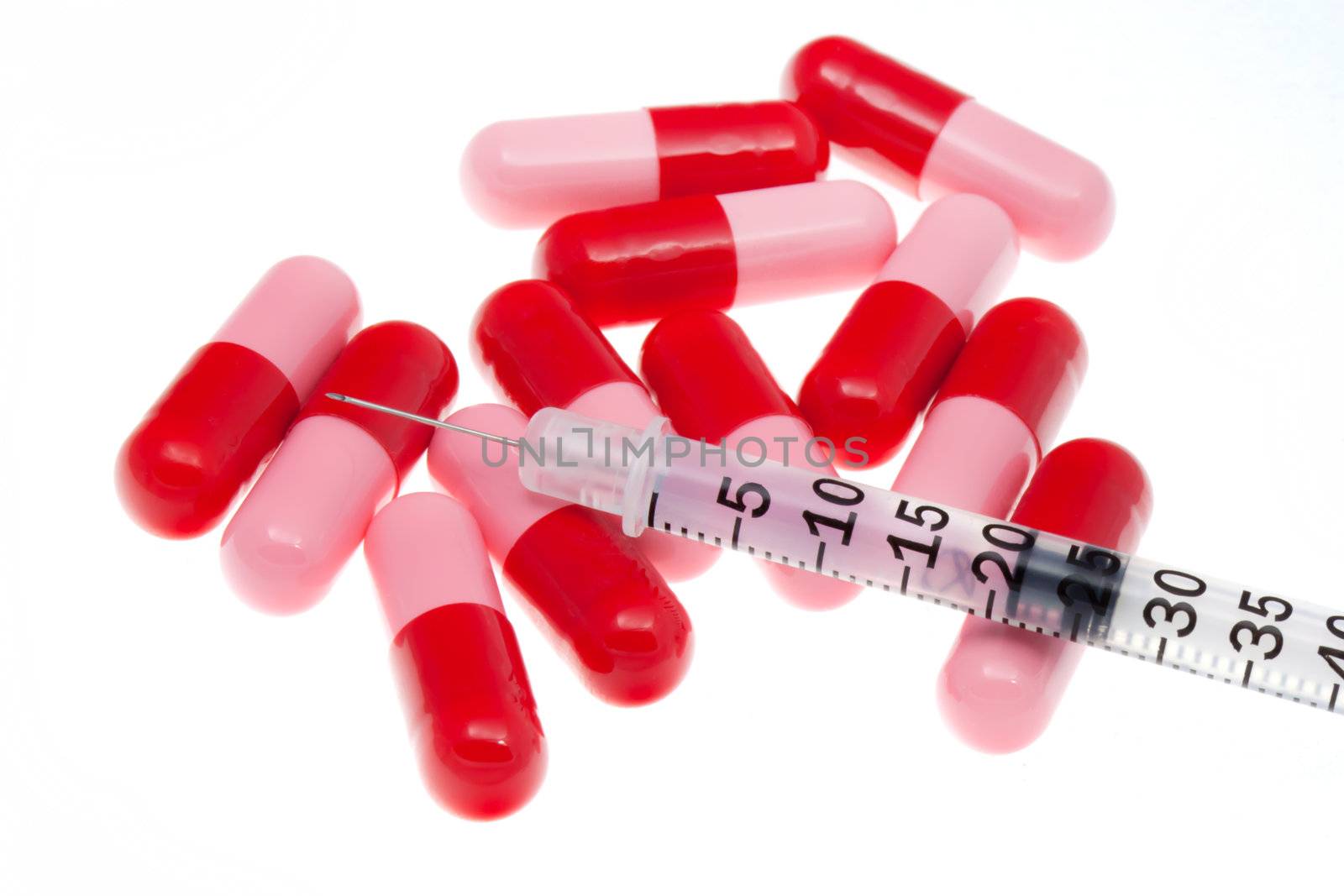 Syringe with red capsules on white background