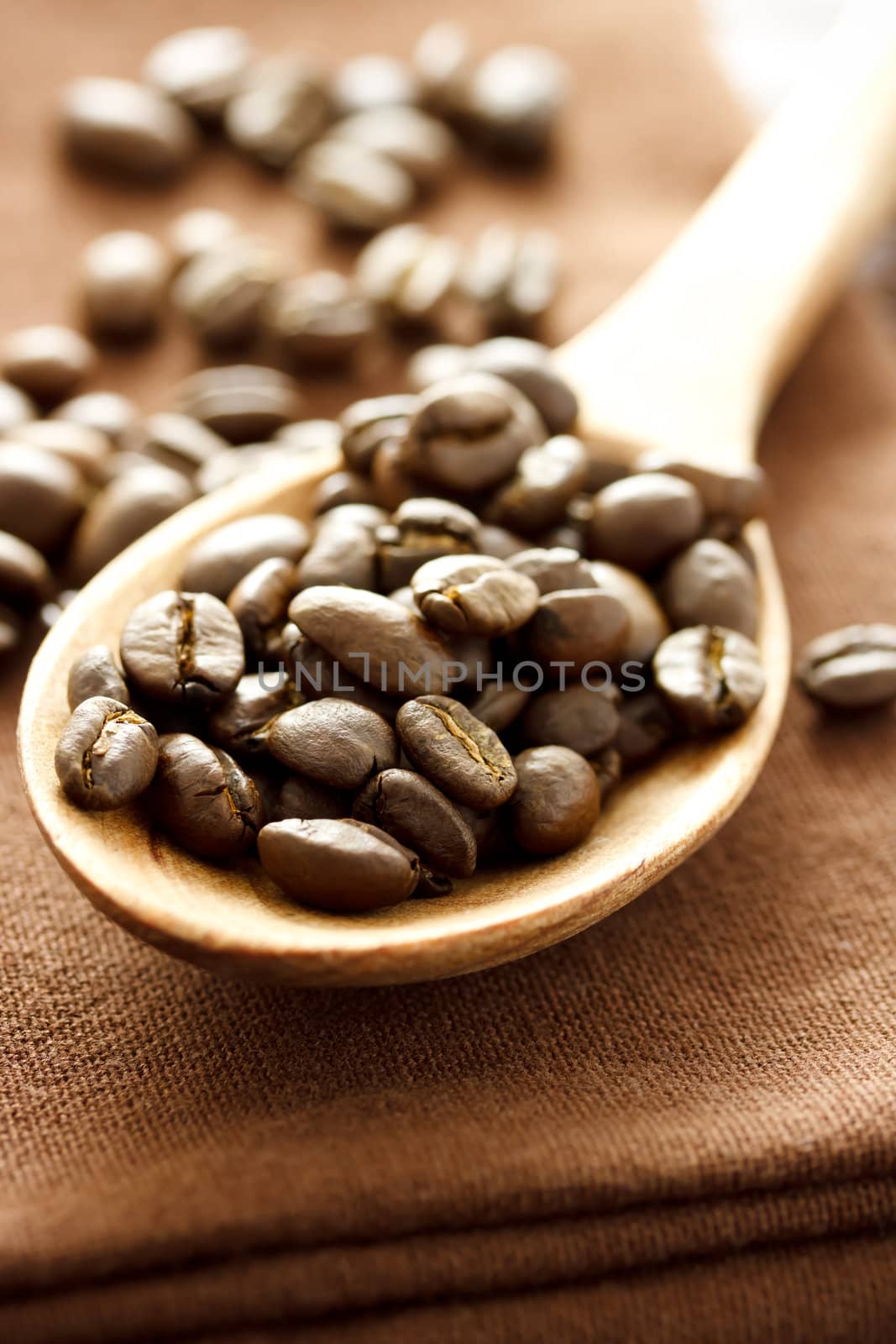 Coffee beans in wooden spoon on brown cloth