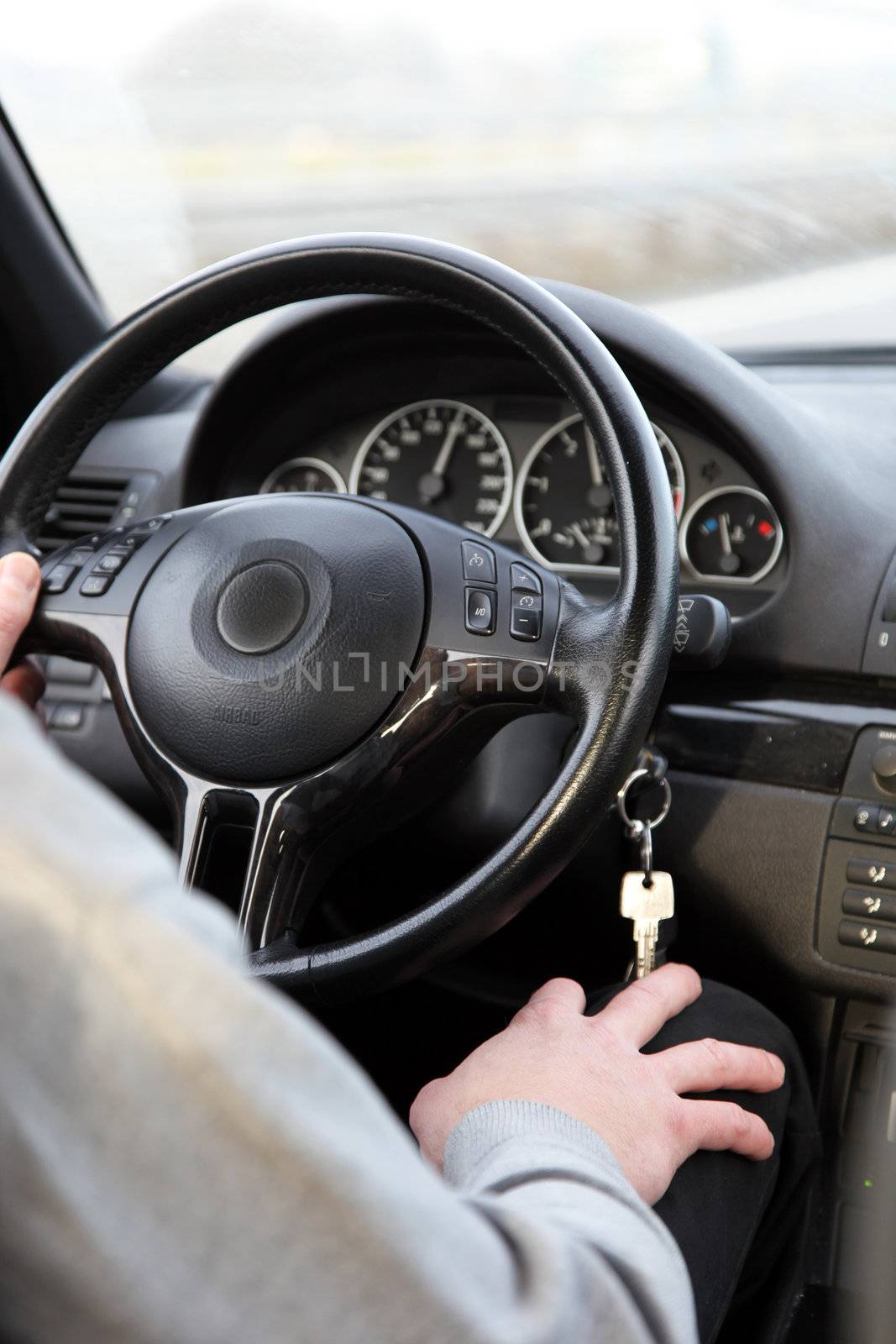Cropped view over the shoulder image of a man driving a car with one hand on the steering wheel and the other on his knee below the dangling ignition key Cropped view overthe shoulder image of a man driving a car with one hand on the steering wheel and the other on his knee below the dangling ignition key - no discernable view through the windscreen