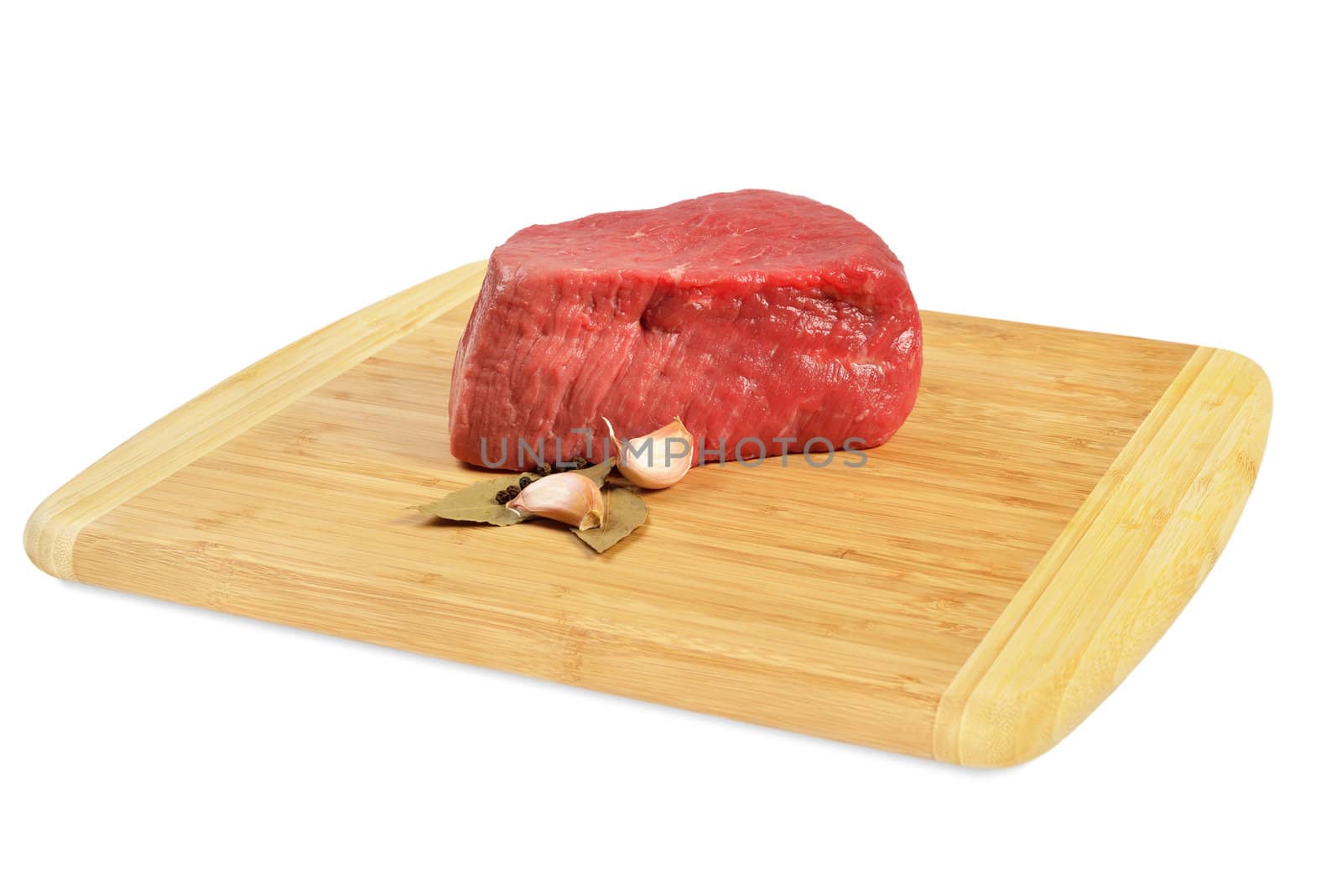 Piece of raw beef on a wooden board, decorated with garlic and bay leaves.