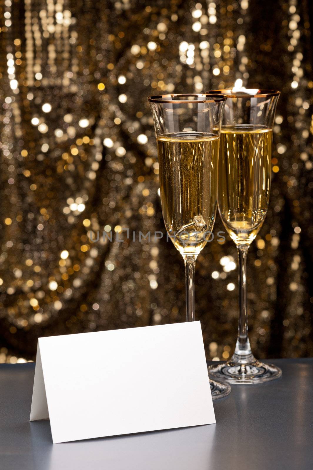 Champagne glasses with submerged ring in front of gold glitter background