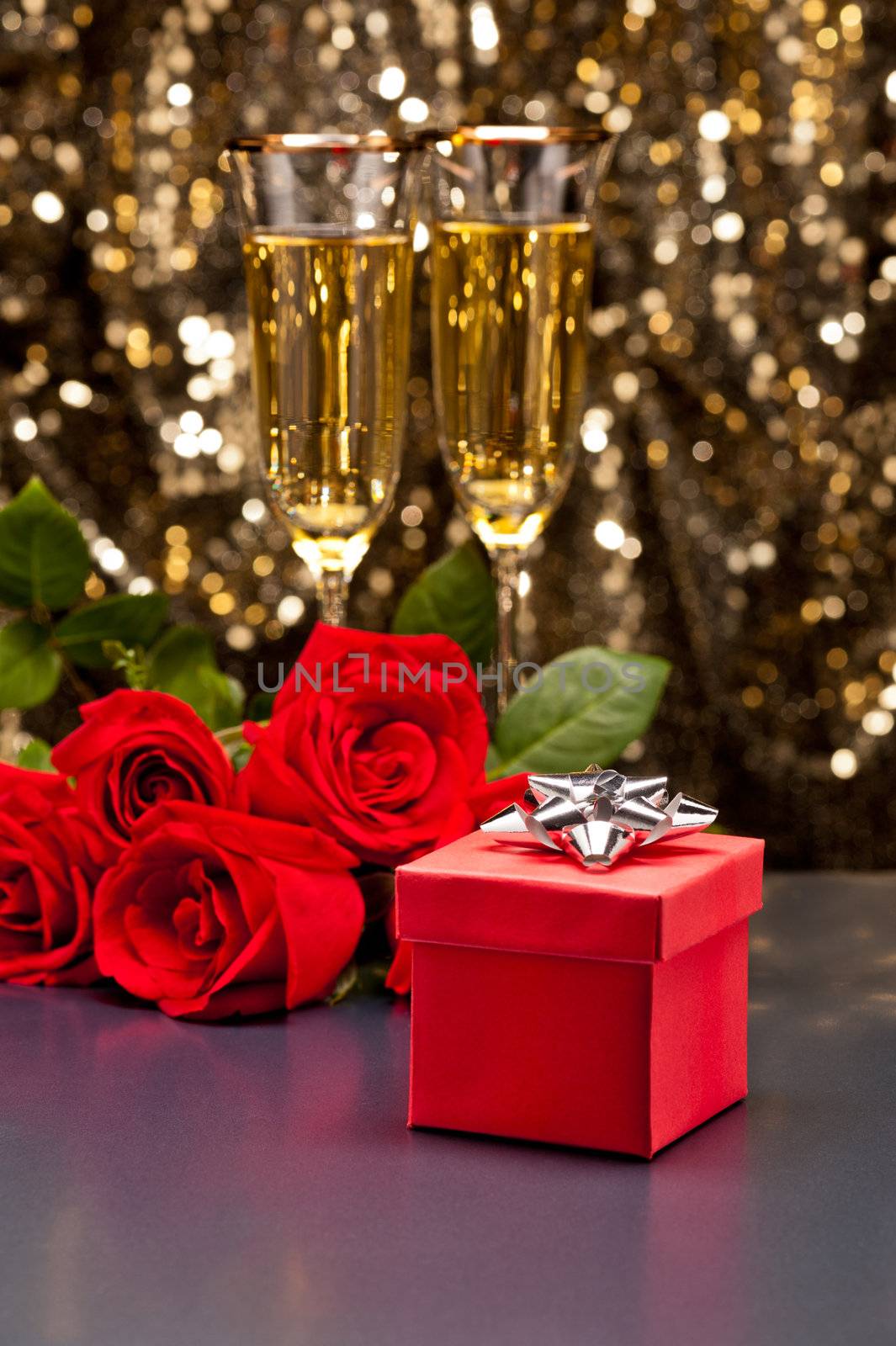 Red present box Champagne and roses in front of a gold glitter background