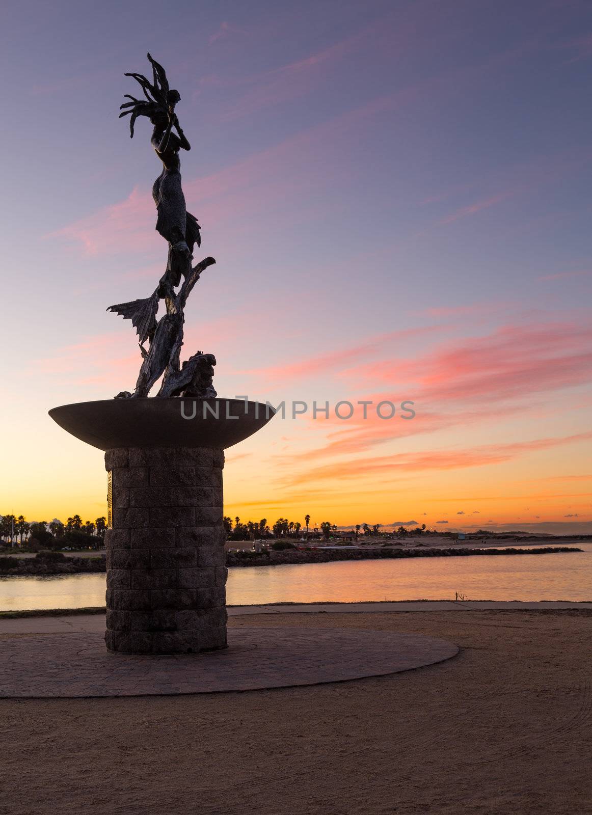 Mermaid statue playing flute by unknown artist at entrance to Ventura Harbor at sunrise