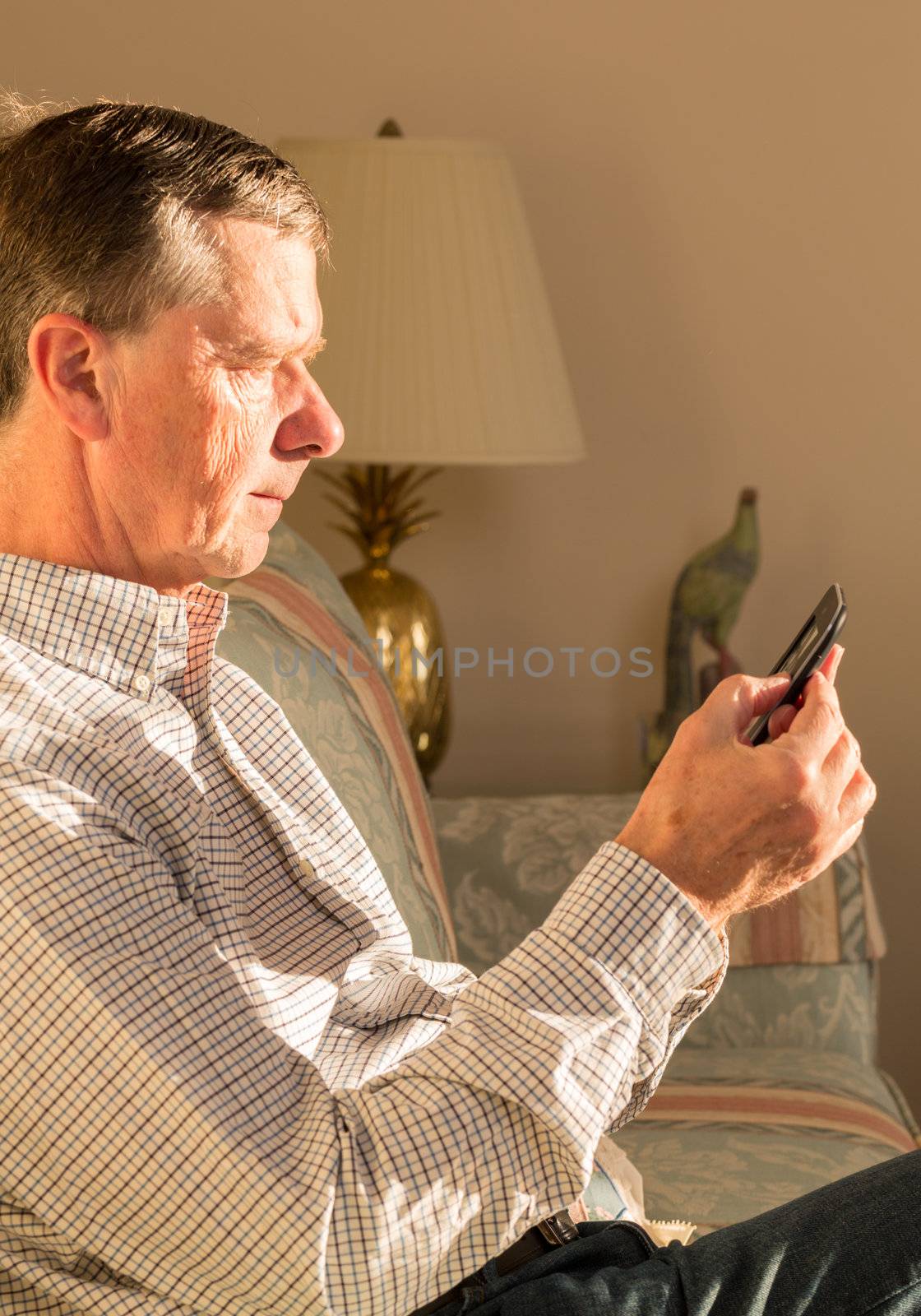 Senior retired man sitting in sunlight reading eBook in living room