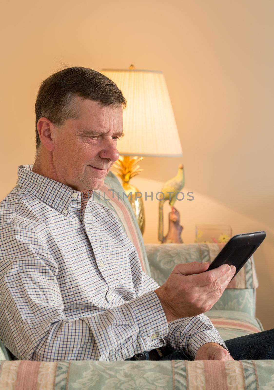 Senior retired man sitting in sunlight reading eBook in living room
