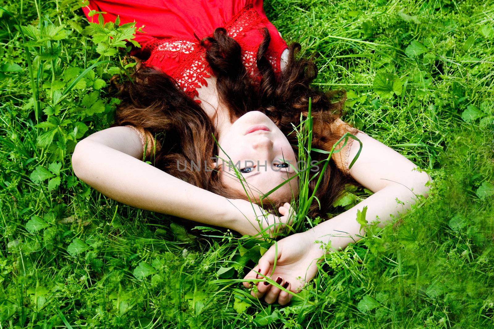 Beautiful girl with blue eyes lying on green grass
