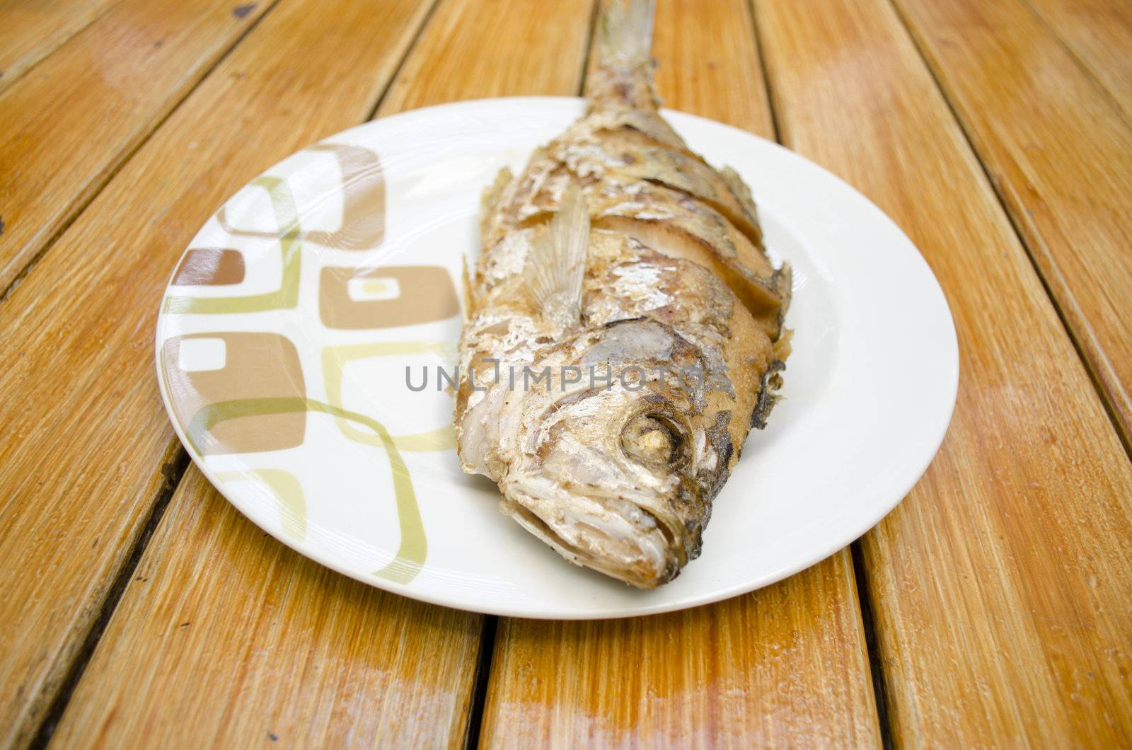 Fried fish on white dish and wood background by siraanamwong