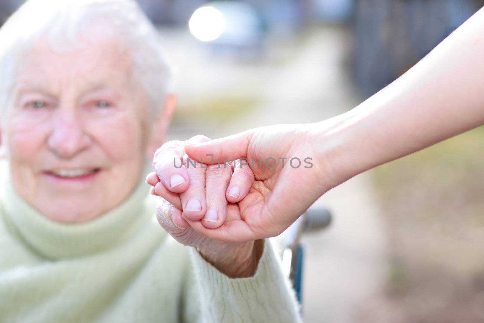 Senior Lady in Wheelchair and Young Woman Holding Hands Outside